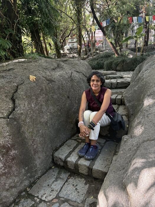 Nitya resting on stone steps in the hills, prayer flags overhead