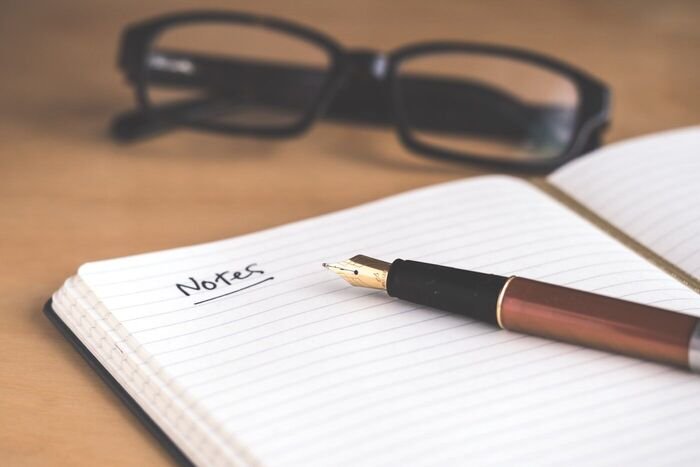 A notebook, fountain pen and glasses on a desk