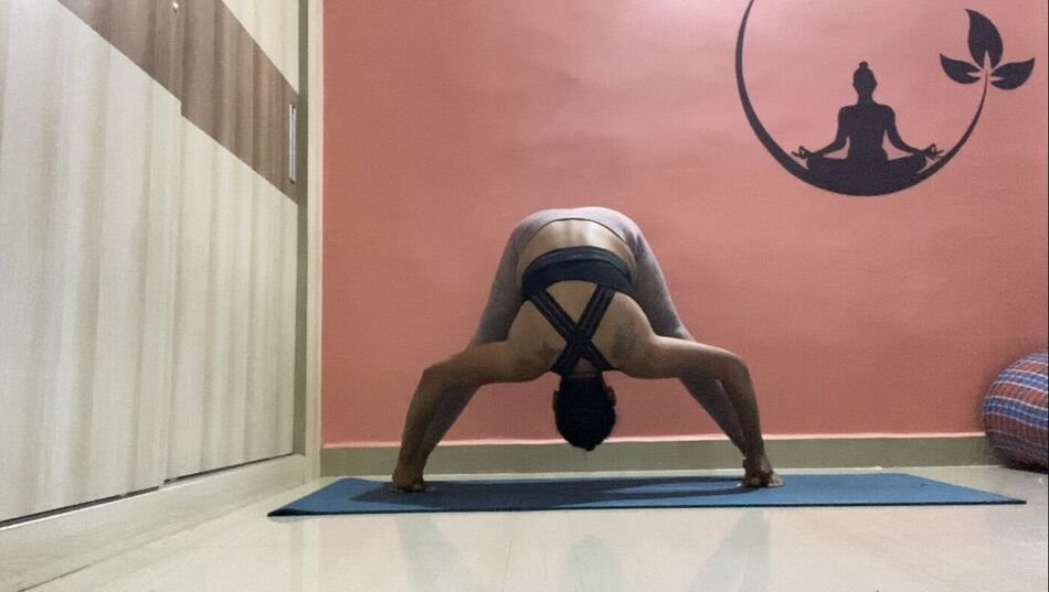 Nitya in Prasarita Padottanasana, a wide-legged forward fold